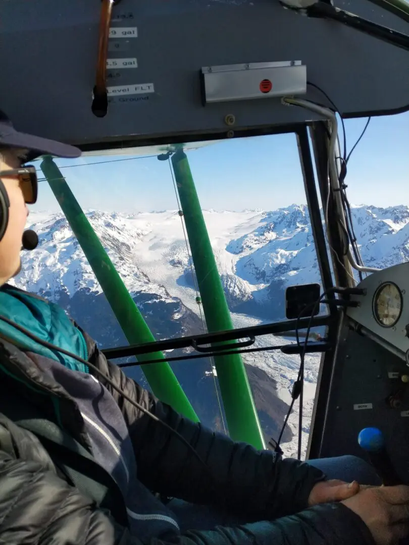 A man sitting in the cockpit of a plane with mountains in the background.