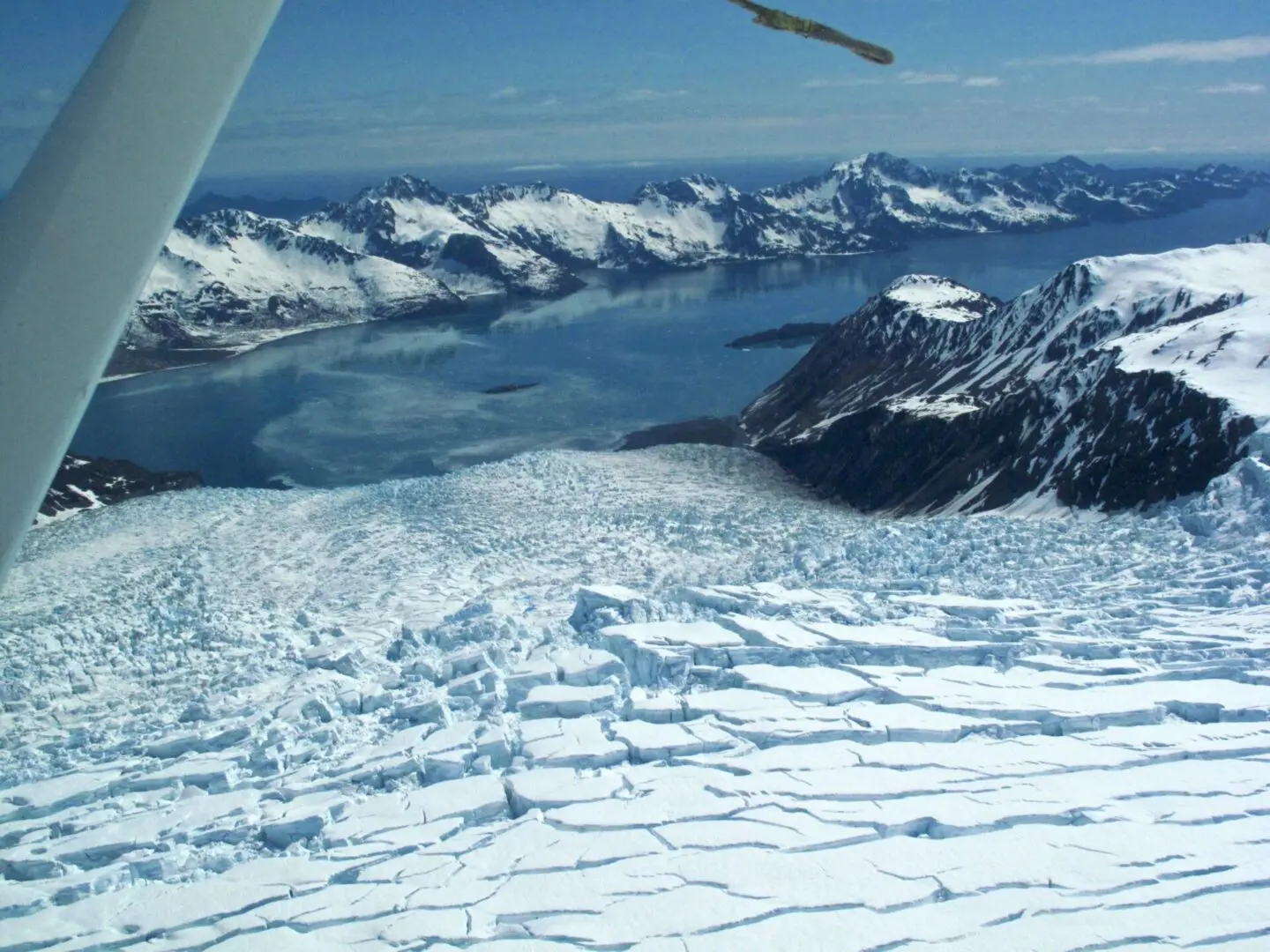 A plane flying over a glacier with mountains in the background.