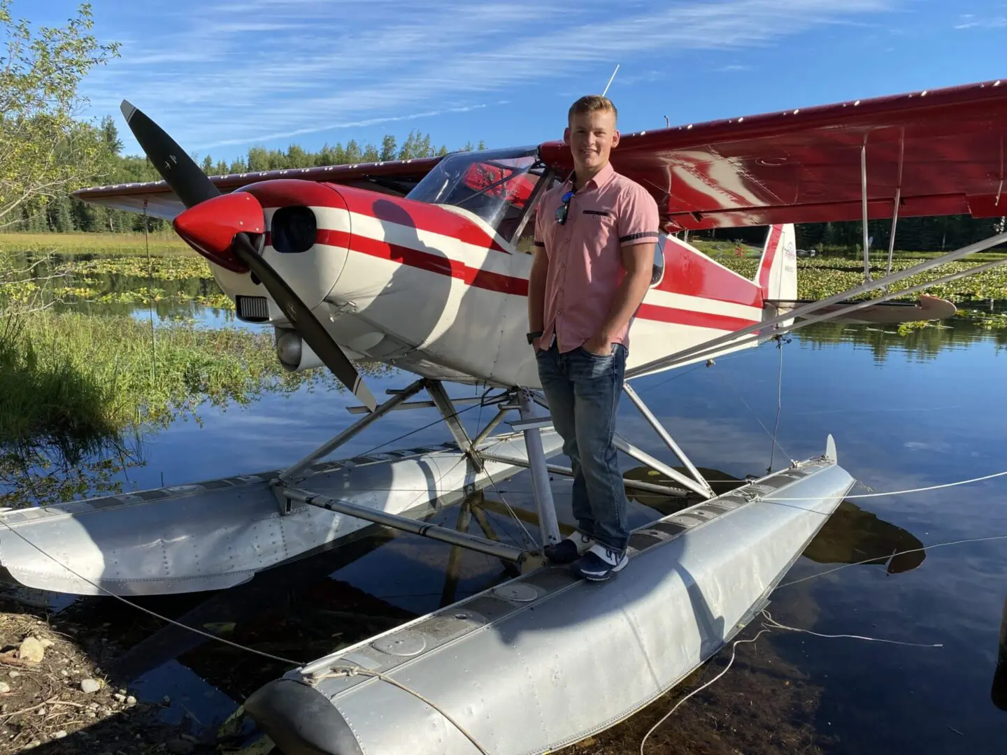 A man standing next to a red and white plane in the water.