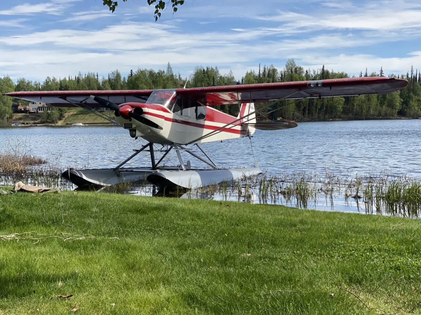 A small plane sits on the grass next to a lake.