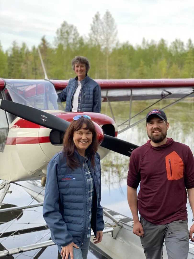 Three people standing in front of a small plane.