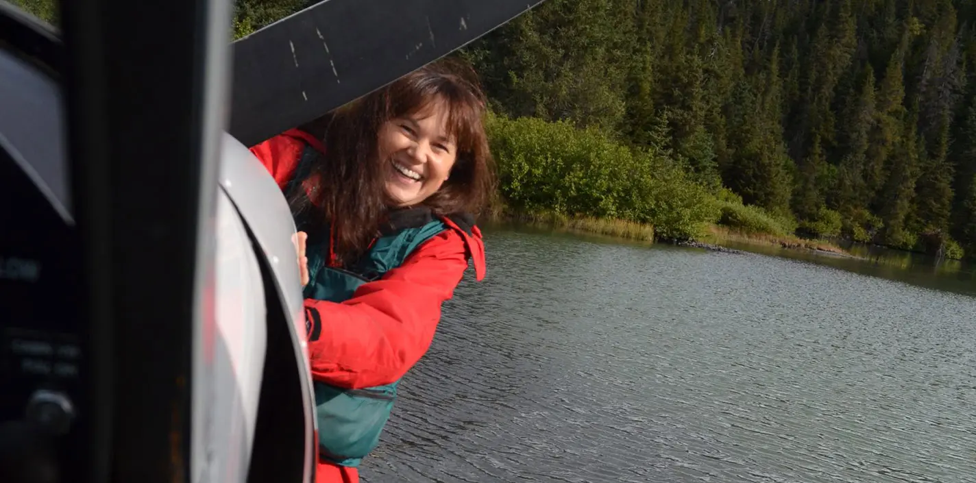 A woman in a red jacket standing next to a boat in a lake.