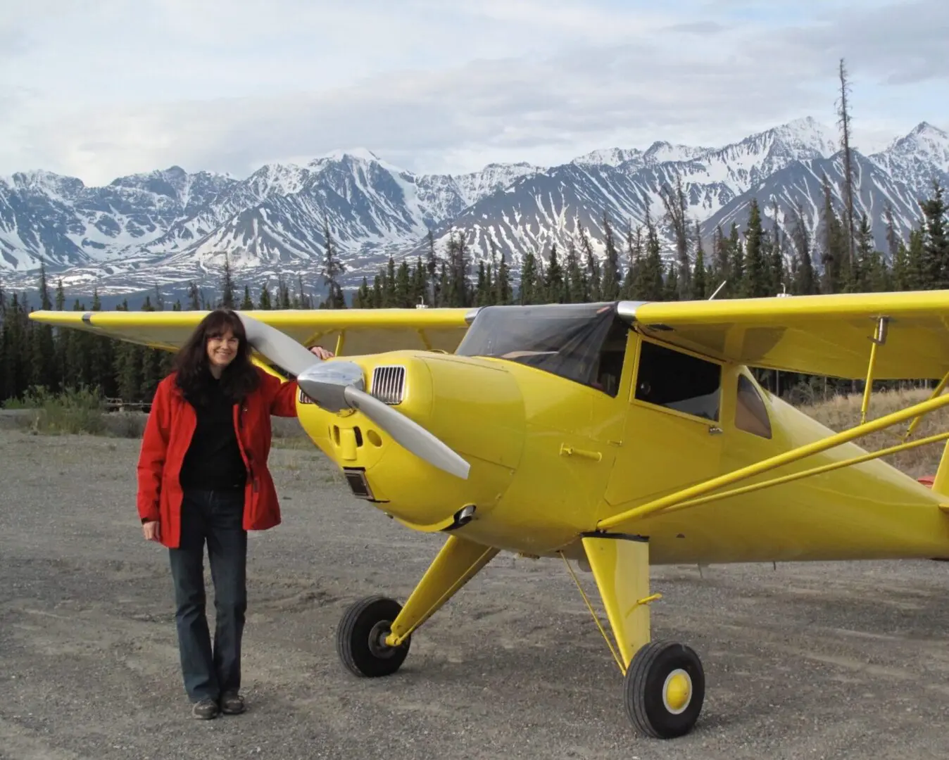 A woman standing next to a yellow airplane.