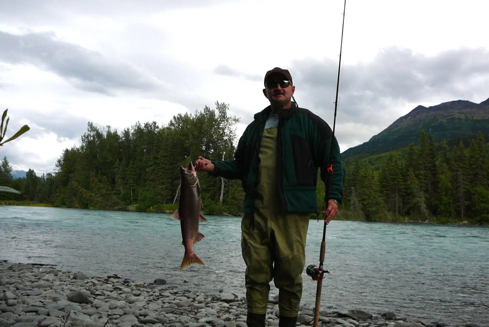 A man holding a fish on a rocky river.