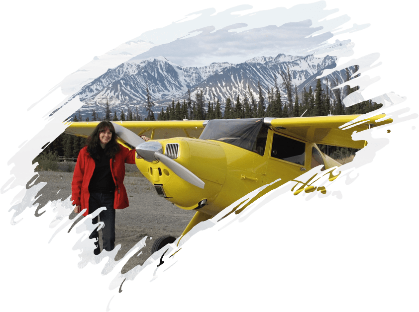 A woman standing in front of a yellow airplane with mountains in the background.