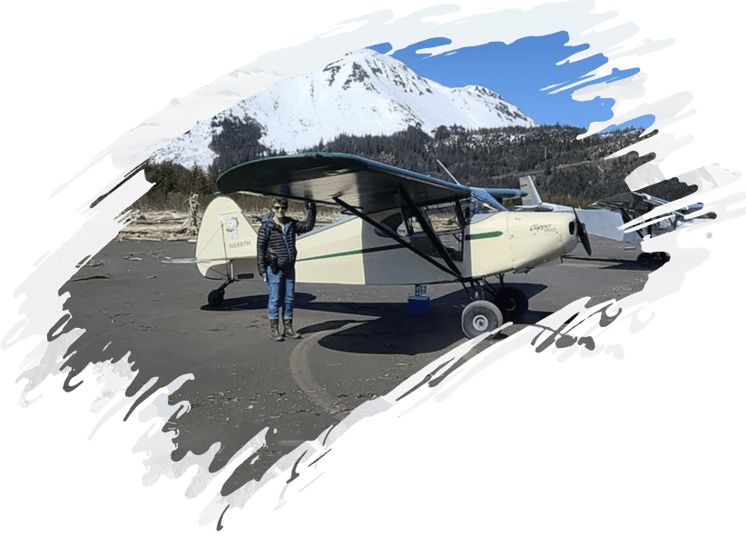 A person standing next to a small plane with mountains in the background.