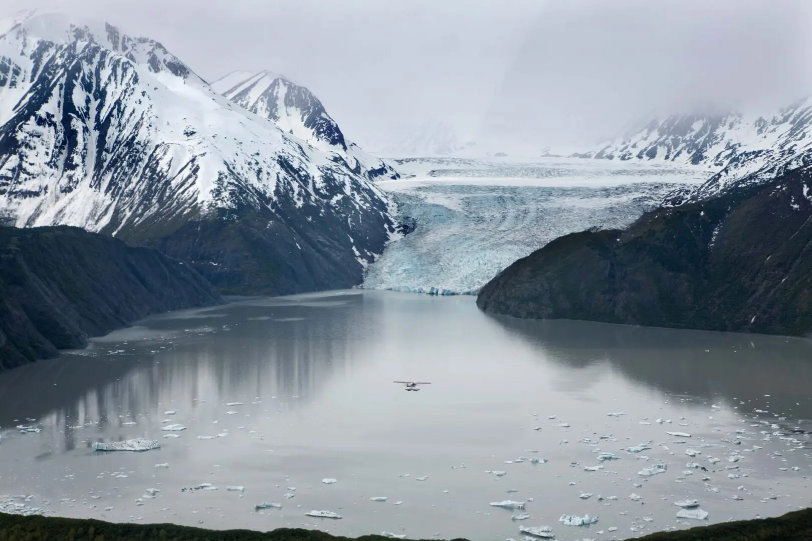 A plane flies over a glacier and icebergs.