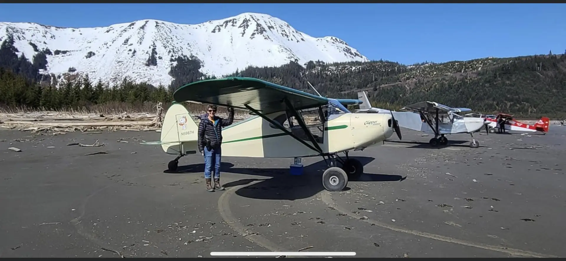 A man is standing next to a small biplane on the beach.